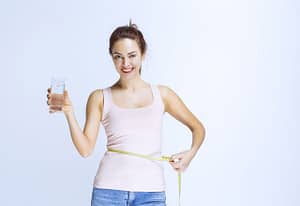 Girl holding a glass of pure water and measuring her waist size